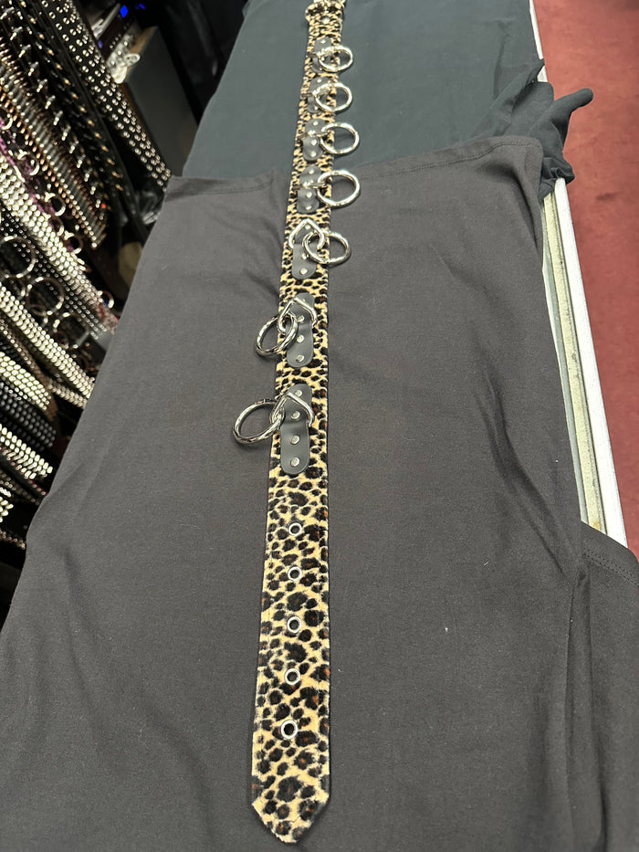 Leopard print tie with metal rings on a gray garment in a store setting