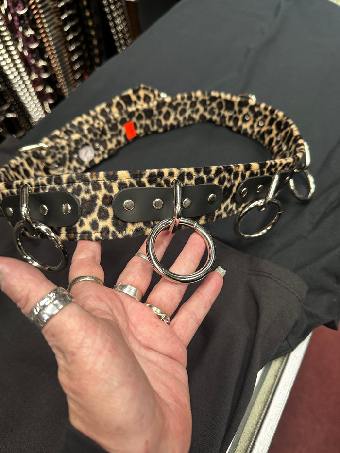 Leopard print belt with metal rings held by a hand on a dark surface