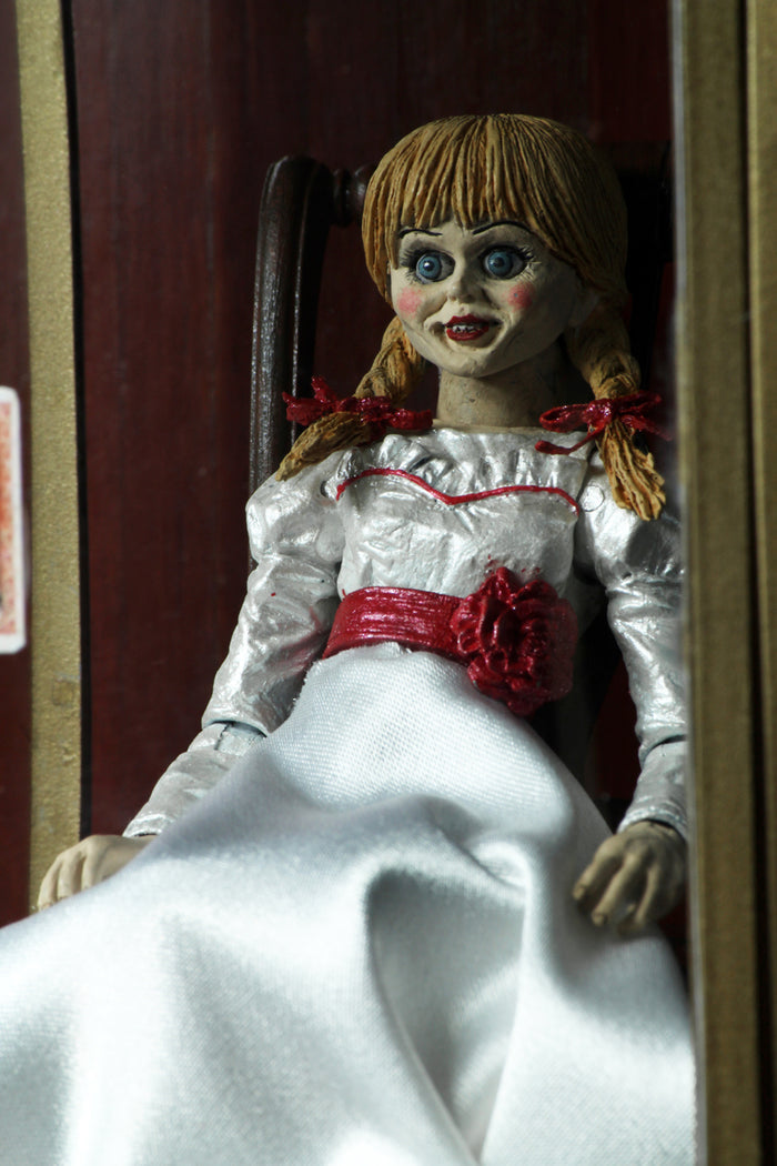 annabelle figure sitting in chair wearing white dress with hair in pig tails. sign reading "warning! positively do not open"