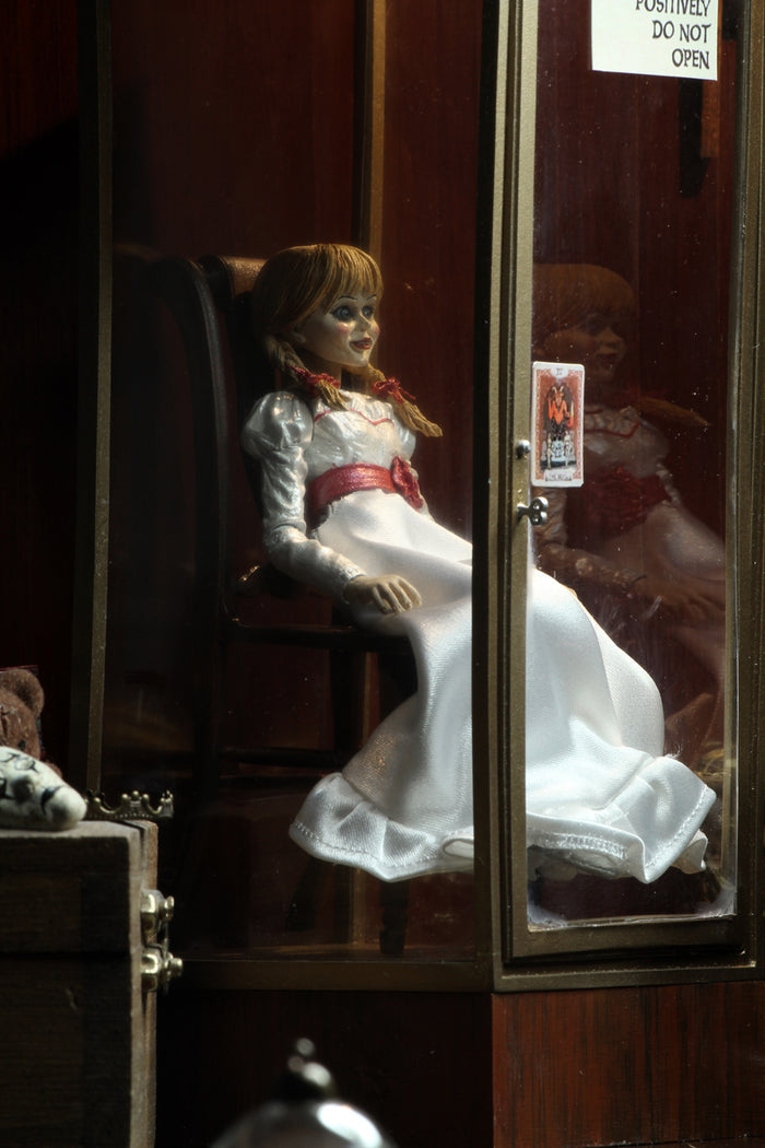 annabelle figure sitting in chair wearing white dress with hair in pig tails. sign reading "warning! positively do not open"