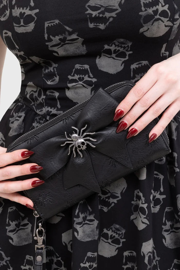 Black clutch with spider embellishment held by a person wearing a black dress with skull pattern.