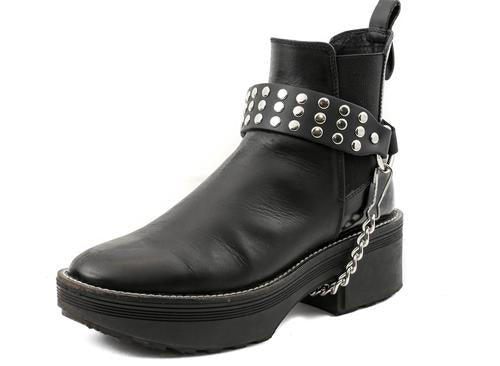 black ankle boot displaying black boot strap with three rows of multiple silver riveted studs and hanging silver chain underneath