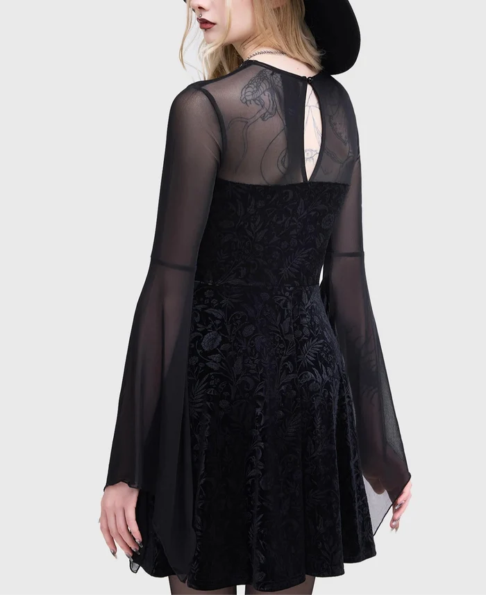 Model wearing a black dress with sheer sleeves and a black hat on a white background