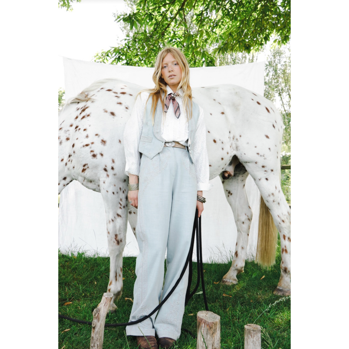women standing in front of a horse wearing a bandana around her neck with light wash denim vest, white blouse and light wash denim jeans