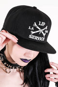 front view of Black hat with white embroidery that reads "LIP SERVICE LA USA" on the front with crossbones. Snaps on the back.