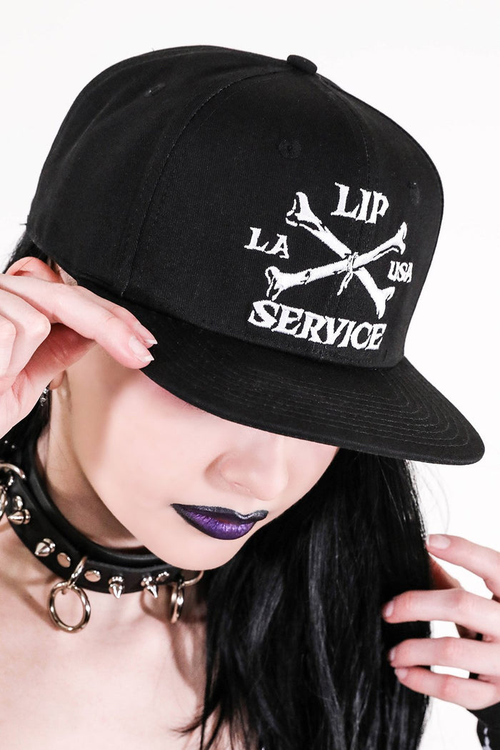 front view of Black hat with white embroidery that reads "LIP SERVICE LA USA" on the front with crossbones. Snaps on the back.