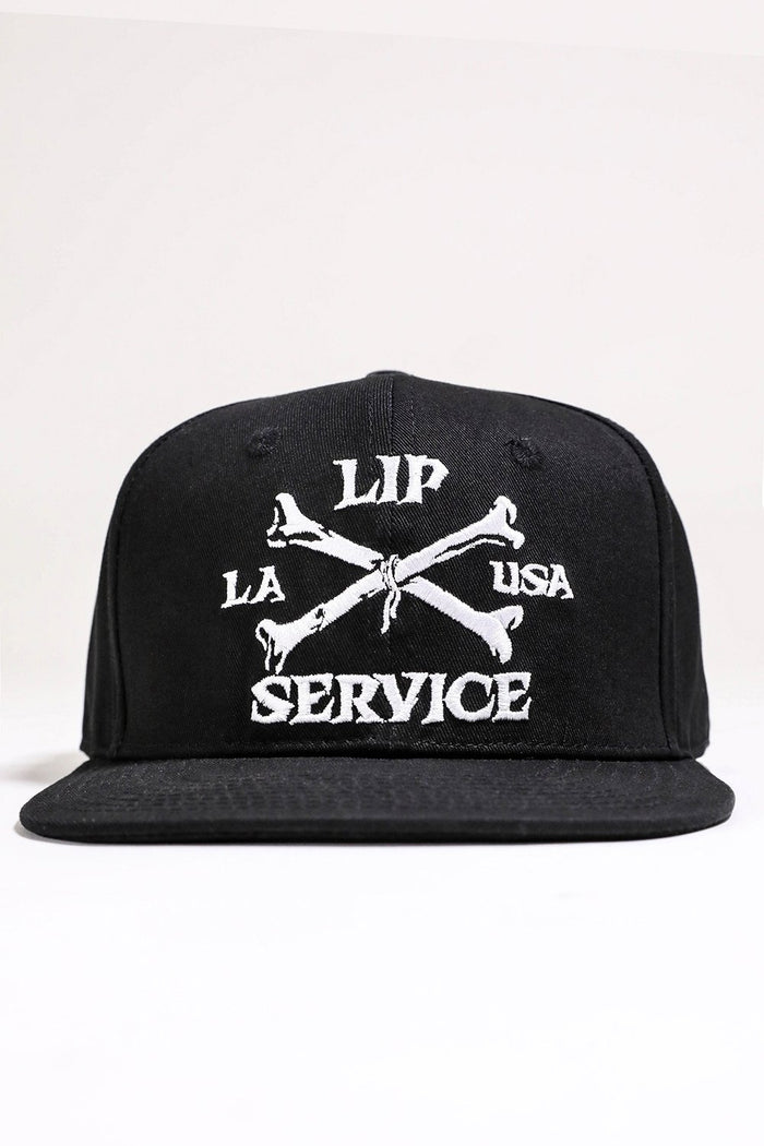 front view of Black hat with white embroidery that reads "LIP SERVICE LA USA" on the front with crossbones. Snaps on the back.
