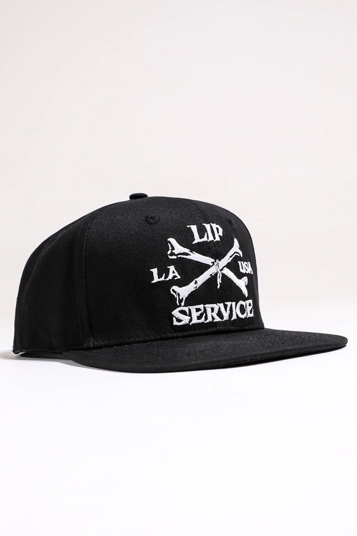 front view of Black hat with white embroidery that reads "LIP SERVICE LA USA" on the front with crossbones. Snaps on the back.