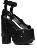 outer view of black vegan leather strappy platform sandal with 6.5" heel. Sandal has gunmetal hardware, adjustable ankle strap and adjustable side strap. Bottom of front platform has a fanned grip for better stability.