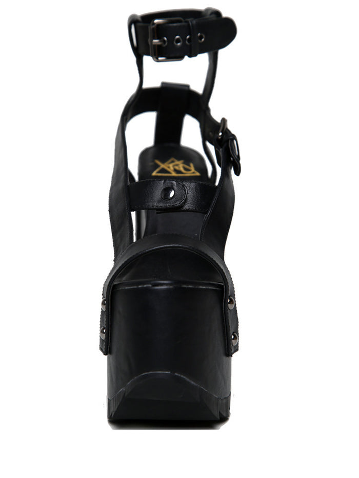 front view of black vegan leather strappy platform sandal with 6.5" heel. Sandal has gunmetal hardware, adjustable ankle strap and adjustable side strap. Bottom of front platform has a fanned grip for better stability.