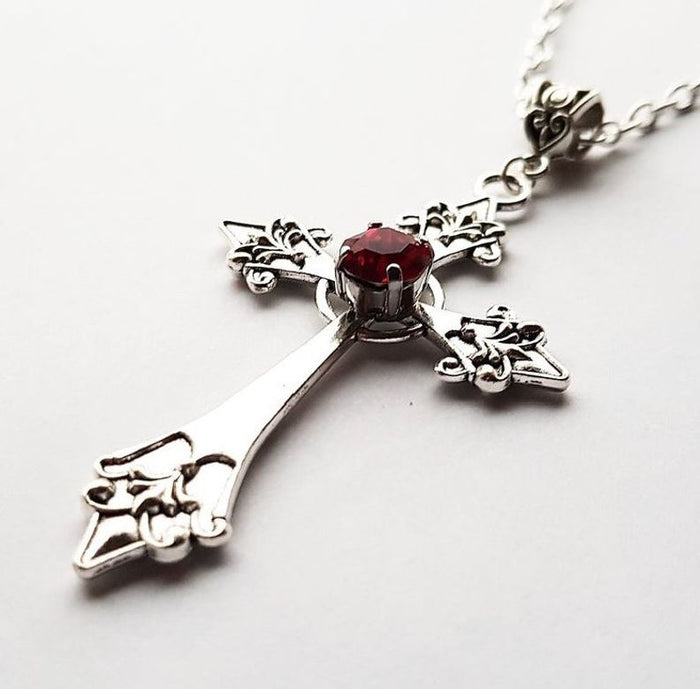 Silver colored zinc alloy vampire cross necklace with red cubic zirconia gem in center of cross.