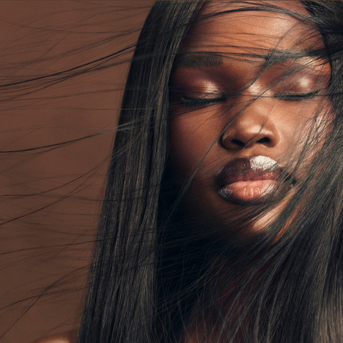 Person with long dark hair with eyes closed against warm-toned background.
