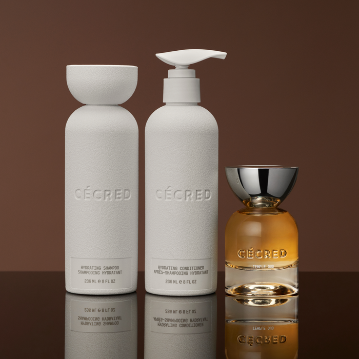 Two white cylindrical bottles labeled hydrating shampoo and conditioner with a golden fragrance bottle featuring a silver cap