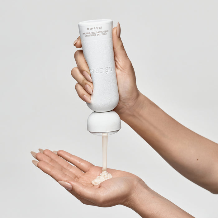 White cylindrical pump bottle dispensing cream into an open hand against a gray background.