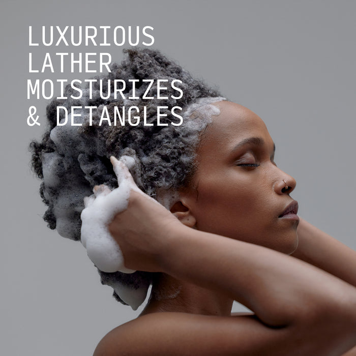 Person applying white lather to textured dark hair and scalp during hair care routine.