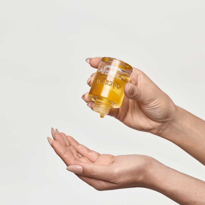 Hands dispensing Cécred Nourishing Hair Oil from the amber glass bottle showing the golden oil formula against a white background