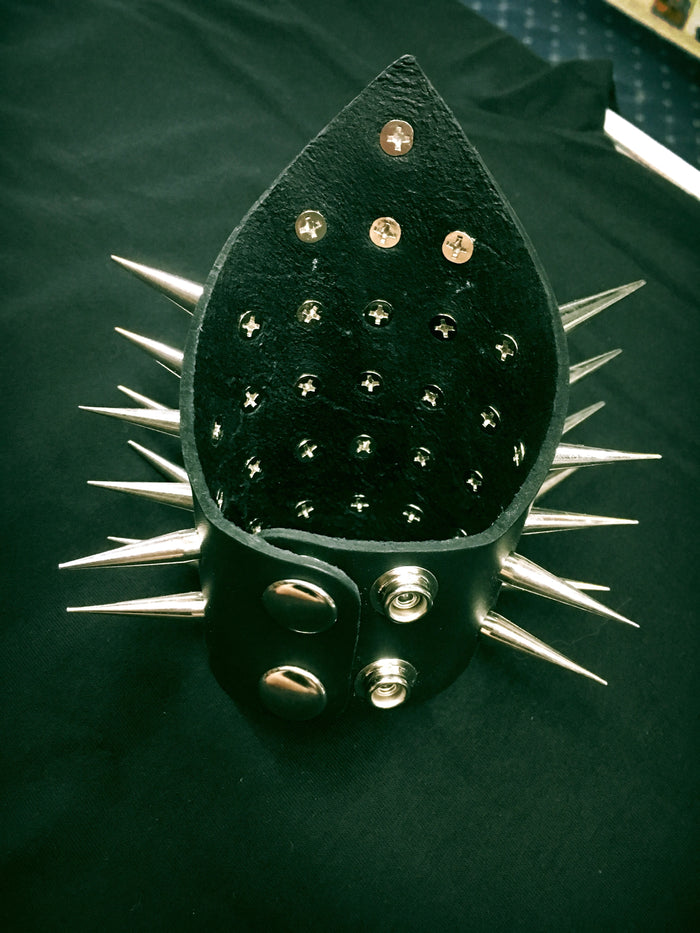 triangular shaped black leather gauntlet bracelet with multiple rows of two inch silver needle spikes. shows snap closure