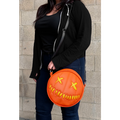 woman wearing bag on shoulder. bag is orange with yellow eyes and yellow teeth, with a black adjustable strap. based on sam's jack o lantern in the movie trick r' treat