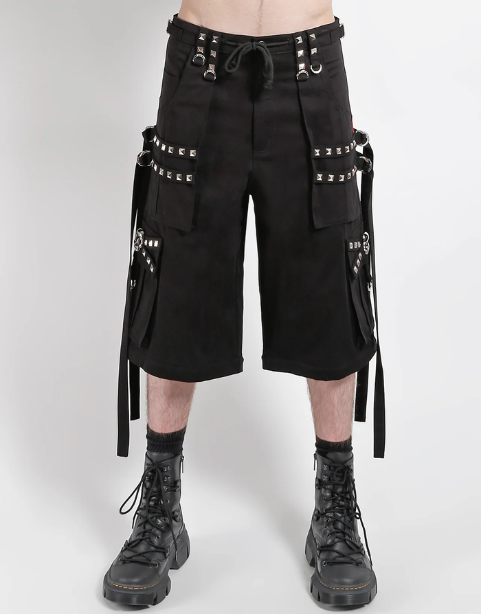 Waist-down view of baggy black punk-style cargo pants featuring silver pyramid studs, hanging side straps, a drawstring waist, and chunky black boots against a white background.