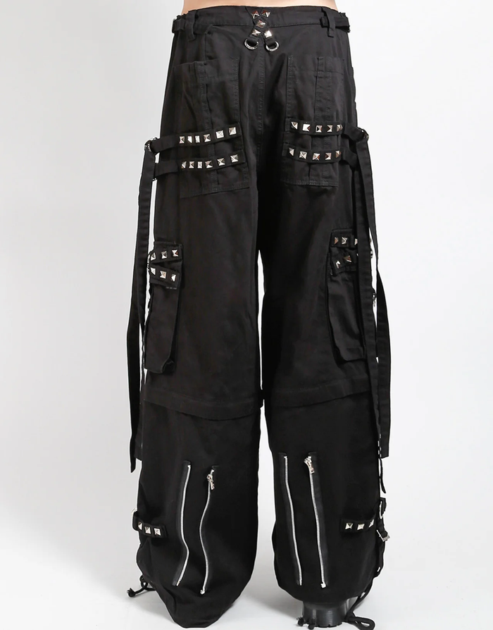 Waist-down view of baggy black punk-style cargo pants featuring silver pyramid studs, hanging side straps, a drawstring waist, and chunky black boots against a white background.