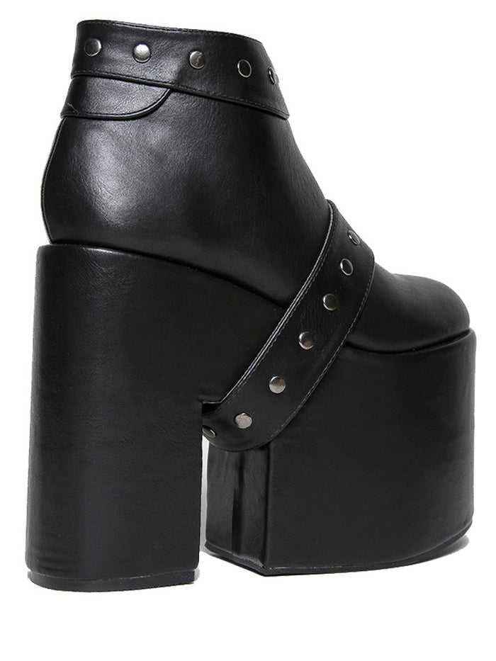 side view of black vegan leather super tall 6" heel, 4" platform sleep design boot. Boot has a rivet studded strap that wraps around and is removable or attachable with Velcro. Boot has black EVA platform.