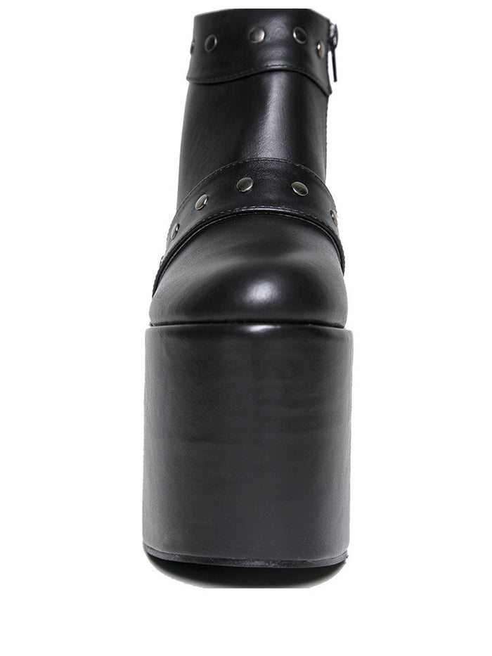 front view of black vegan leather super tall 6" heel, 4" platform sleep design boot. Boot has a rivet studded strap that wraps around and is removable or attachable with Velcro. Boot has black EVA platform.