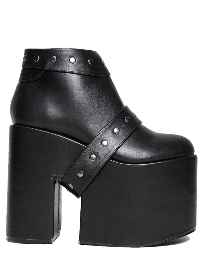 side view of black vegan leather super tall 6" heel, 4" platform sleep design boot. Boot has a rivet studded strap that wraps around and is removable or attachable with Velcro. Boot has black EVA platform.