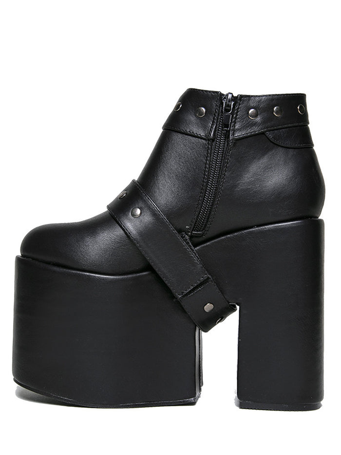 inner side view of black vegan leather super tall 6" heel, 4" platform sleep design boot. Boot has a rivet studded strap that wraps around and is removable or attachable with Velcro. Boot has black EVA platform.