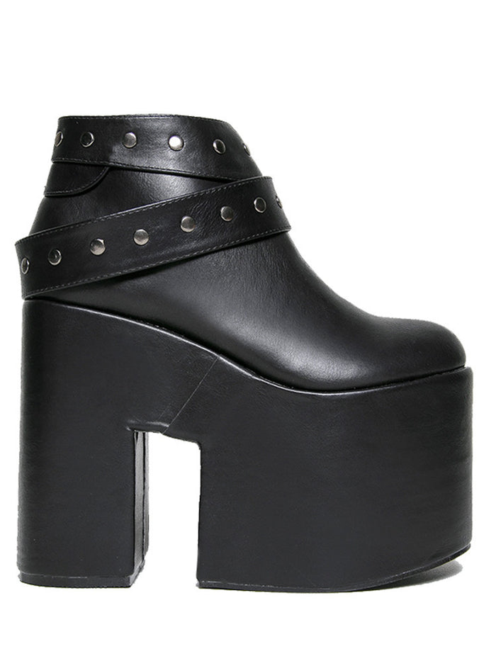 outer side view of black vegan leather super tall 6" heel, 4" platform sleep design boot. Boot has a rivet studded strap that wraps around and is removable or attachable with Velcro. Boot has black EVA platform.
