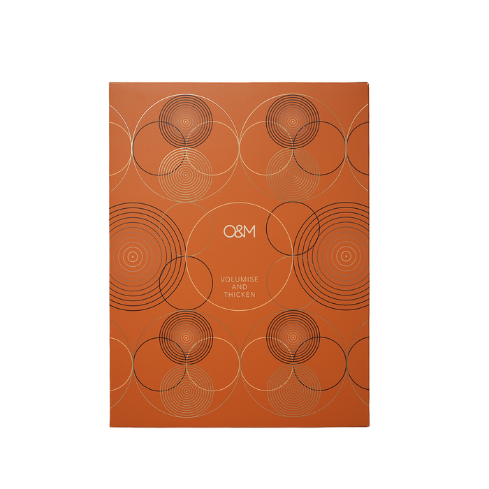 A rectangular orange box with a geometric pattern of overlapping circles in black and light beige lines, featuring the text 'O&M VOLUMISE AND THICKEN' in the center, shown on a plain white background.