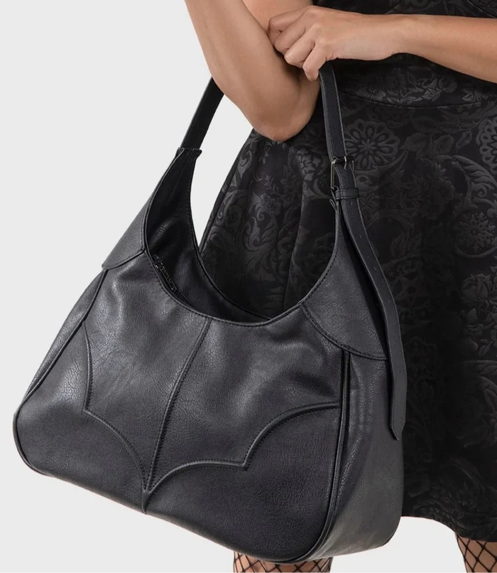 model wearing a black lace dress and black hat holding a black handbag on a white background