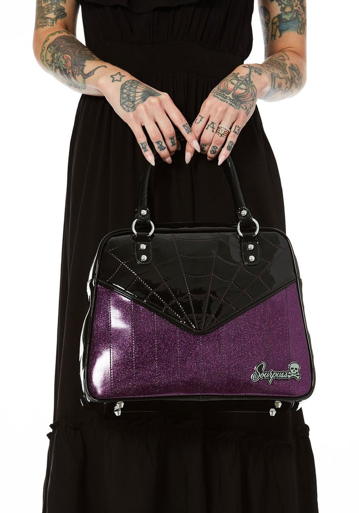 Glossy black vinyl and purple stitched spider webbing, along with contrast purple glitter panel with backseat stitching. Generously sized and can double as an overnight bag, complete with satin leopard liner and signature metal Sourpuss emblem and reinforced studded handles.